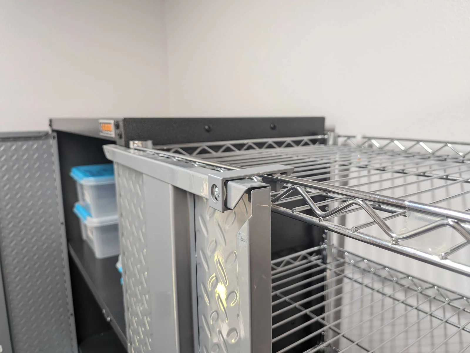 Gray printed clip holding a storage-cabinet door open against an adjacent chrome wire shelf