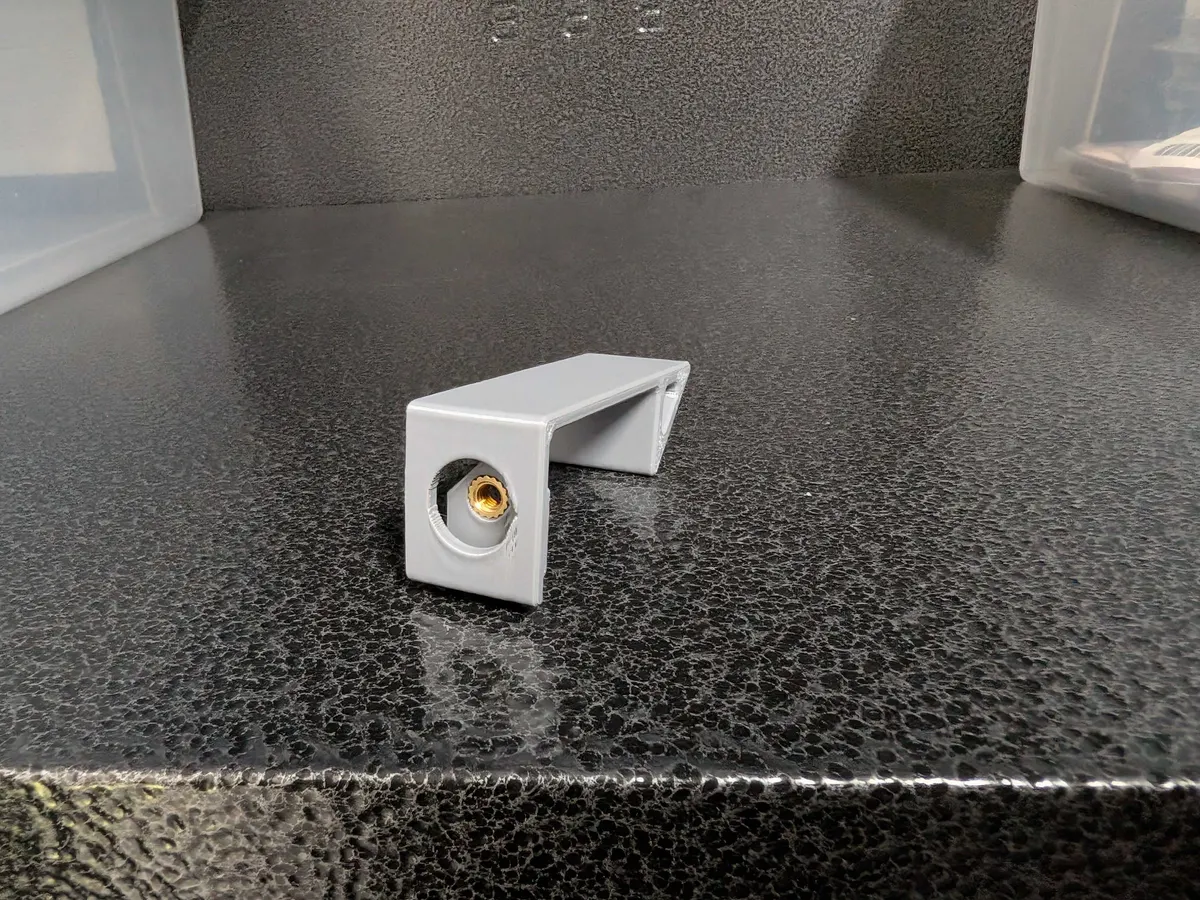 Isolated gray door clip showing its threaded brass insert and hooked profile